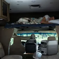 Un homme dort dans un camping-car 4 places. Une unité de climatisation portable et une station d'énergie sont visibles.