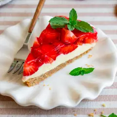 Ein Stück köstlicher Erdbeerkuchen ohne Backen, garniert mit frischer Minze, auf einem weißen Teller.