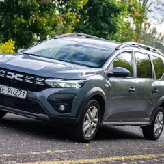 Szare auto 7 osobowe Dacia Jogger na tle zieleni. Idealne na rodzinne wycieczki.