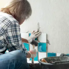 Fachowiec układa płytki w łazience. Zastanawiasz się, ile bierze fachowiec za remont łazienki?
