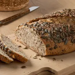 Chleb z mąki orkiszowej, posypany pestkami dyni i sezamu, pokrojony na desce.