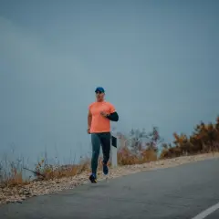 Mężczyzna w pomarańczowej koszulce i czapce biega po pustej drodze. Czy można biegać na czczo? To pytanie zadaje sobie wielu sportowców.