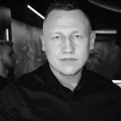 DJ Iroon w czerni, gotowy do rozkręcenia imprezy. W tle neonowe światła klubu.