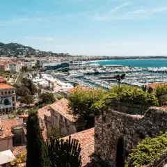 Widok na port w Cannes z licznymi jachtami i budynkami. W oddali wzgórza porośnięte zielenią.