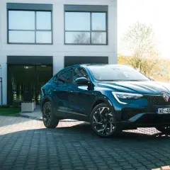 Elegancki, granatowy Renault Arkana na tle nowoczesnego budynku. Sprawdź, jaka jest jego renault arkana cena i możliwości.