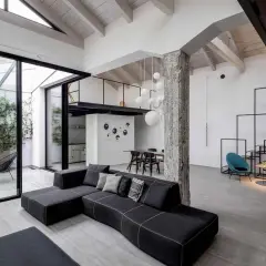 Un ampio soggiorno con tetto a vista e un soppalco, che mostra cos'è un loft: spazio aperto, design industriale e un tocco di verde da un patio interno.