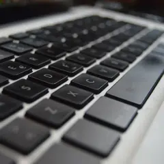 Zbliżenie na klawiaturę laptopa, widoczne klawisze z literami i cyframi. Ustawienie klawiszy jest standardowe, gotowe do pisania.