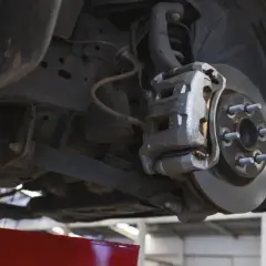 Widok od spodu na zawieszenie samochodu z widocznym zaciskiem hamulcowym i tarczą. Może to być przyczyna metalicznego dźwięku podczas jazdy.