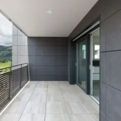 Nowoczesny balkon z jasnymi kaflemi na podłodze i szarymi płytami na ścianach. Widok na zielone wzgórza i miasto.