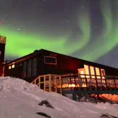 En snöig sluttning leder upp till en mysig aurora sky station. Norrskenet dansar grönt över stjärnorna.