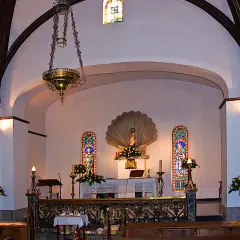 Interior de la iglesia de conchas Galicia, con altar, vitrales y lámpara colgante.