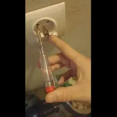 Próbnik świeci na bolcu gniazdka elektrycznego, sprawdzając napięcie.