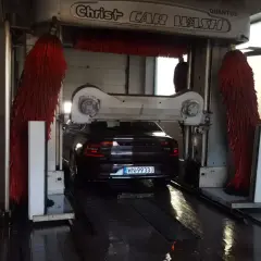 Czarny Volvo wjeżdża do myjni automatycznej. Czerwone szczotki są gotowe do czyszczenia samochodu.