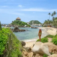 Mujer en bikini admira una playa paradisíaca con palmeras y un kiosko en una isla, ideal para un viaje a Colombia.