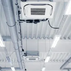 Conductos de ventilación y unidades de aire acondicionado de un sistema VRV, iluminados por luces fluorescentes en un techo industrial.