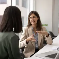 Two women in a meeting. One explains a concept, perhaps what OCB is, with animated hand gestures.