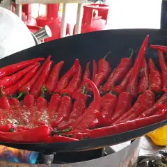 Viele rote Chilis brutzeln in einer Pfanne über offenem Feuer. Wenn der Chili zu scharf ist, was tun? Vielleicht mehr Öl hinzufügen?
