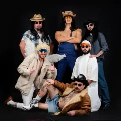 Un gruppo di amici, tra cui un angelo con ali e un cowboy, posa per una foto. Sembrano un gruppo di "ken la fen" pronti per una festa.