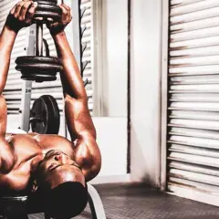Un homme fait un exercice de pull over muscu avec un haltère sur un banc de musculation.