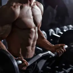 Uomo muscoloso in palestra esegue curl con bilanciere. Quante serie per gruppo muscolare sono necessarie per ottenere un fisico scolpito come questo?