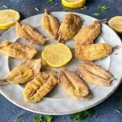 Bocartes fritos crujientes y dorados, servidos en un plato con rodajas de limón y perejil fresco. ¡Un manjar listo para disfrutar!