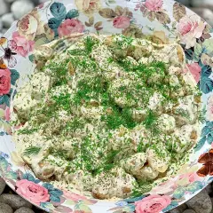 Enkel potatissallad med krämig crème fraiche, toppad med färska örter. Serveras i en vacker skål med blomstermönster.