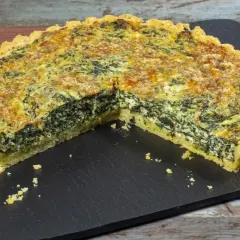 Una fetta di torta salata ricotta e spinaci, con crosta dorata e ripieno cremoso, servita su una lavagna scura.