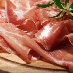 Cienkie plastry prosciutto crudo, ułożone na drewnianej desce, z gałązką rozmarynu. Pyszne, prawda?