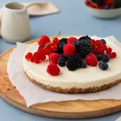 Kalter Hund: Ein cremiger Käsekuchen mit Beeren-Topping, serviert auf einem Holzbrett.