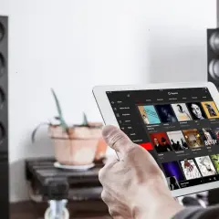Mann sucht auf einem Tablet nach neue Musik. Im Hintergrund stehen zwei schwarze Lautsprecher.