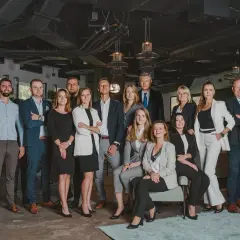 Grupa profesjonalistów w eleganckich strojach pozuje do zdjęcia w nowoczesnym biurze.