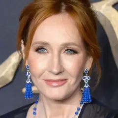 J.K. Rowling, która stworzyła postać Harry'ego Pottera, z niebieskimi oczami i rudymi włosami, w eleganckich, niebieskich kolczykach.