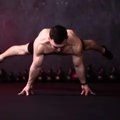 Mężczyzna wykonuje planche, balansując na dłoniach z wyprostowanymi nogami.