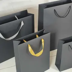 Cztery eleganckie torby papierowe szare, różnej wielkości, z uchwytami z szarej, białej i złotej wstążki.