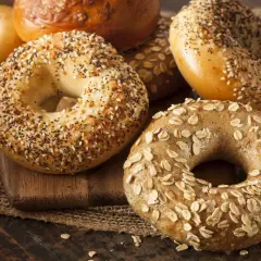 Un assortiment de bagels chauds, certains garnis de graines de sésame et de pavot, d'autres d'avoine, sur une planche en bois.