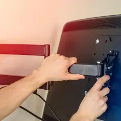 Montaż uchwytu do telewizora. Dwie ręce przykręcają element mocujący do tylnej części ekranu.