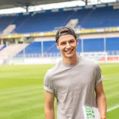 Junger Mann mit Kappe und Buch im Stadion, bereit für seinen Eventmanagement Master.