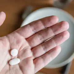 Dłoń trzymająca dwie białe tabletki: okrągłą i owalną.