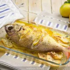 Besugo al horno con patatas y limón, recién sacado del horno en una fuente de cristal.