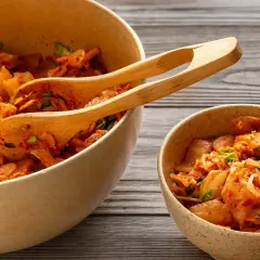 Två skålar med kryddig, fermenterad mat, troligen kimchi, med träskedar i den större skålen.