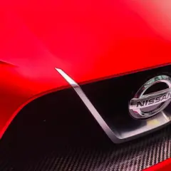 Czerwony Nissan z błyszczącym logo. To jaka to marka? Widać fragment maski i grill z włókna węglowego.