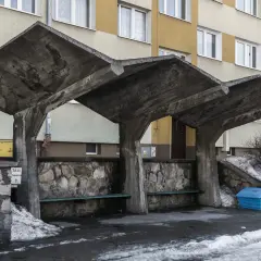 Surowa, betonowa wiata przystankowa, przykład brutalizmu w sztuce, z kamiennym murem i ławkami.
