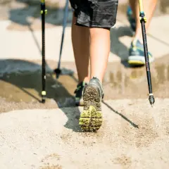 Nordic walking - jak chodzić, żeby schudnąć. Dwie osoby maszerują z kijkami po wilgotnym, piaszczystym podłożu.