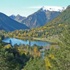 El estany de Llebreta, un lago alpino rodeado de bosques otoñales y montañas nevadas, ofrece una vista serena y colorida.