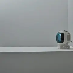 Posąg Buddy medytuje obok retro telewizora, który emituje niebieskie światło. Obok stoi kamera, jakby nagrywała ten niezwykły budda film.