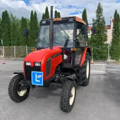 Czerwony traktor Zetor z literą "L" na niebieskiej tablicy, symbolizujący naukę jazdy. Kategoria t prawo jazdy.