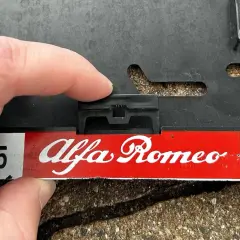 Palec naciska na zatrzask, pokazując, jak zdjąć tablice rejestracyjne z ramki Alfa Romeo.