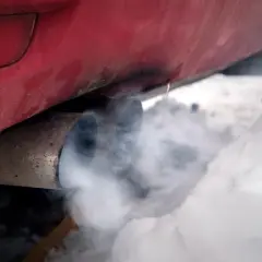 Roter Auspuff mit Rauch im Schnee. Der Motor läuft, um das Auto im Winter warm zu halten.