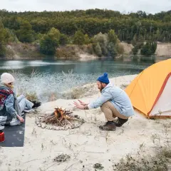 Para spędza wakacje pod namiotem nad jeziorem, rozpalając ognisko.