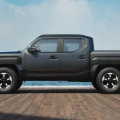 Nowy Kia Tasman, ciemnoszary pickup, stoi na drewnianym molo przy spokojnym morzu.